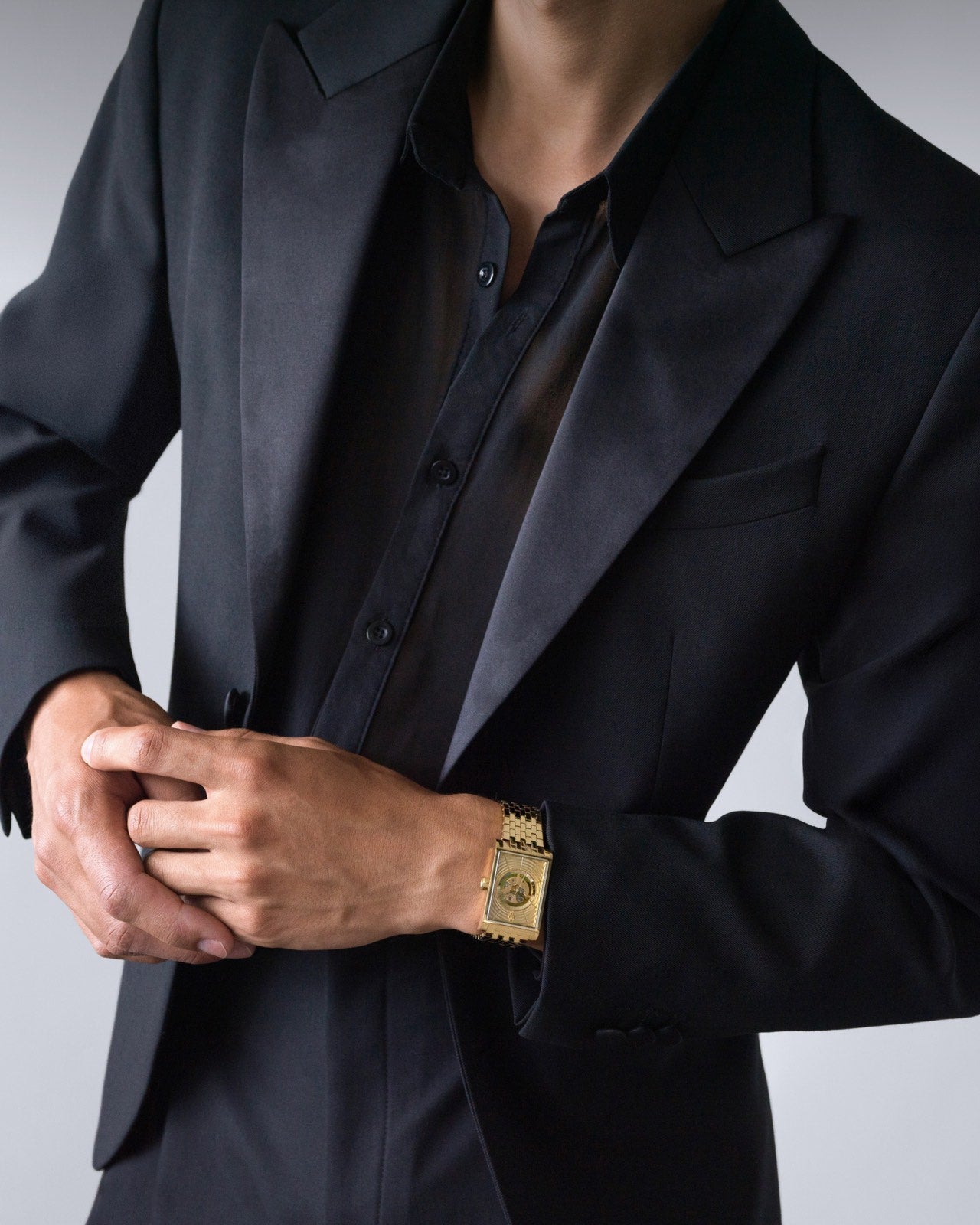 Swiss luxury gold mens rectangular watch on wrist with black blazer and shirt