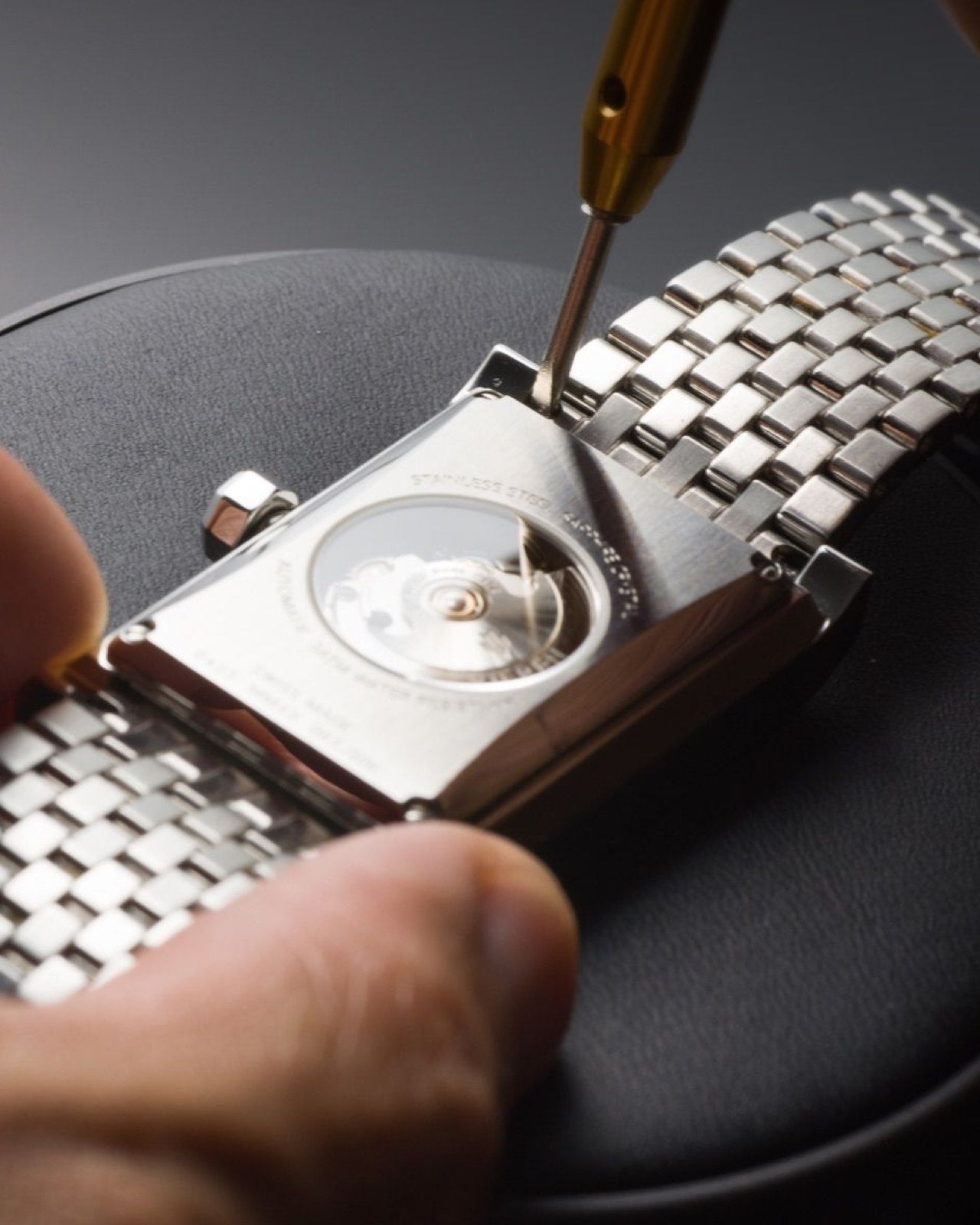 Swiss automatic watch rectangular caseback with screwdriver being serviced by Swiss watchmaker