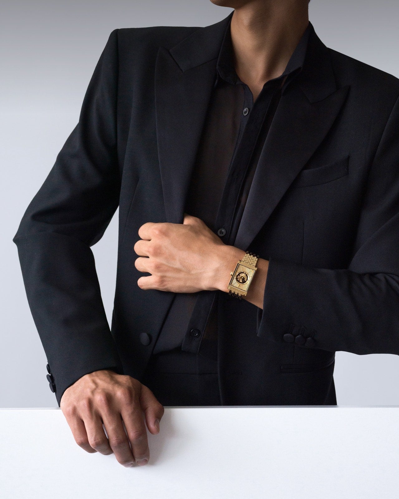 Swiss automatic luxury gold rectangular men’s watch styled with a black shirt and blazer