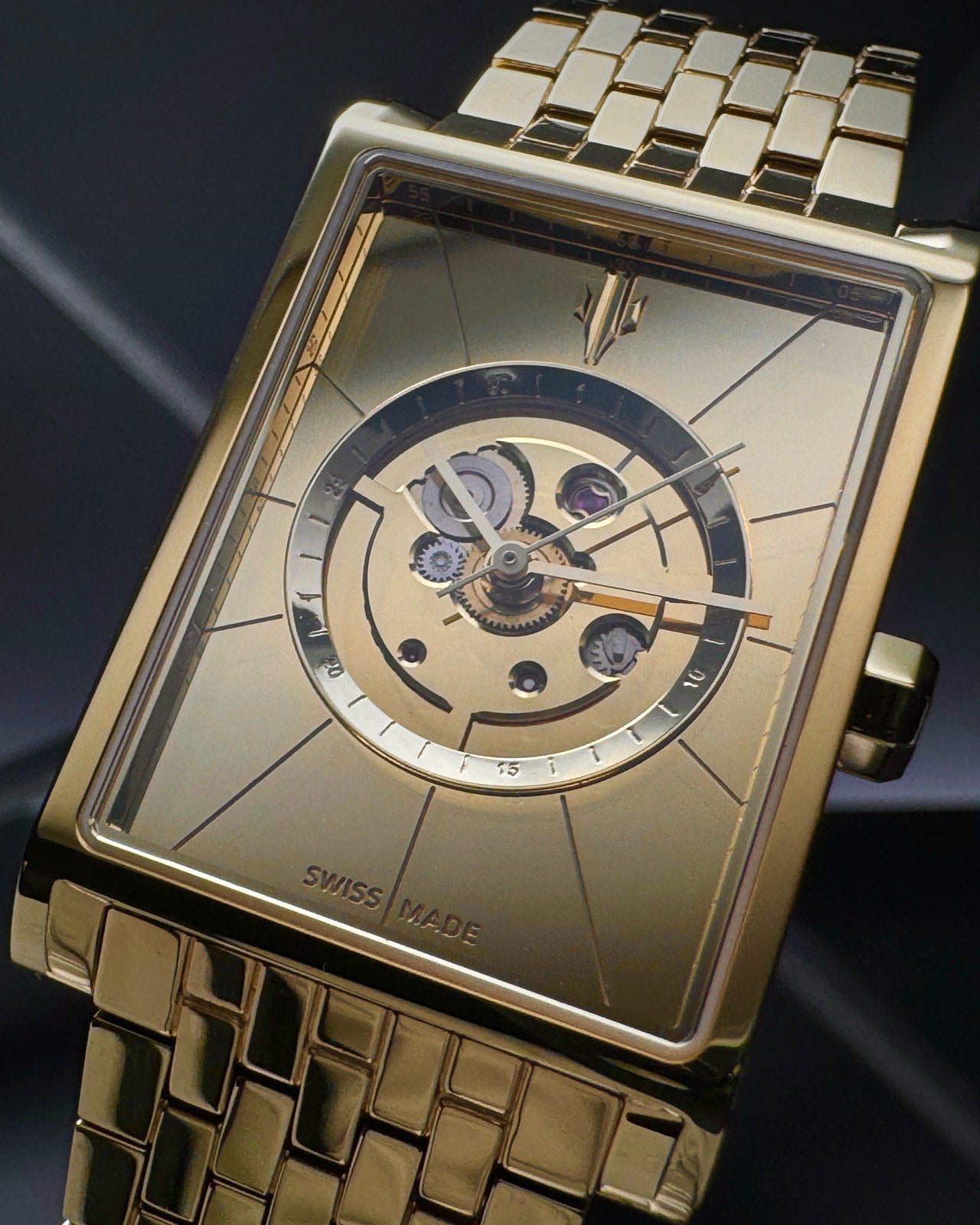 Closeup of gold rectangular watch with skeleton dial and visible jewels of Swiss automatic movement