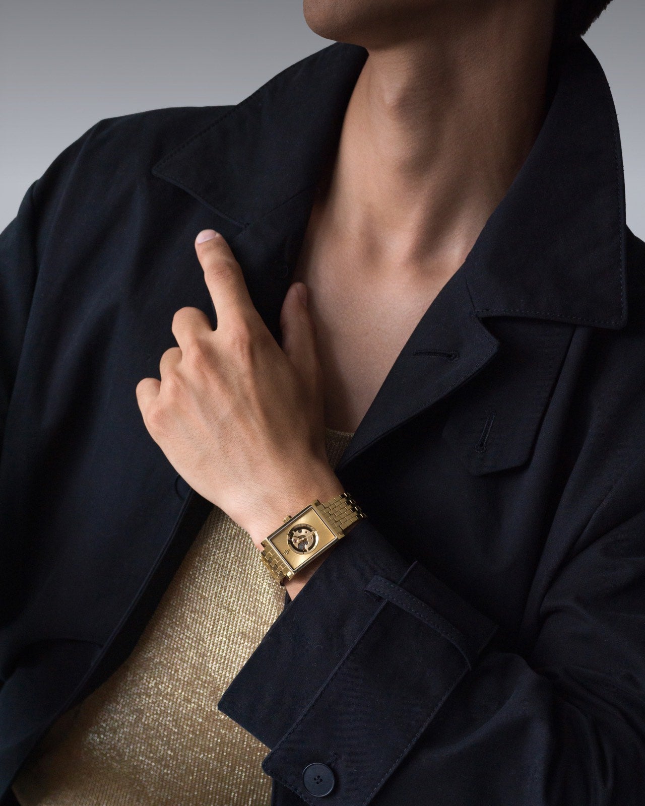Swiss luxury rectangular men’s gold watch on wrist styled with black jacket