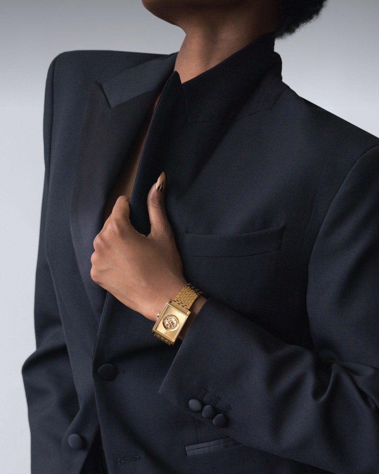 Swiss luxury rectangular women’s gold watch on wrist with black blazer