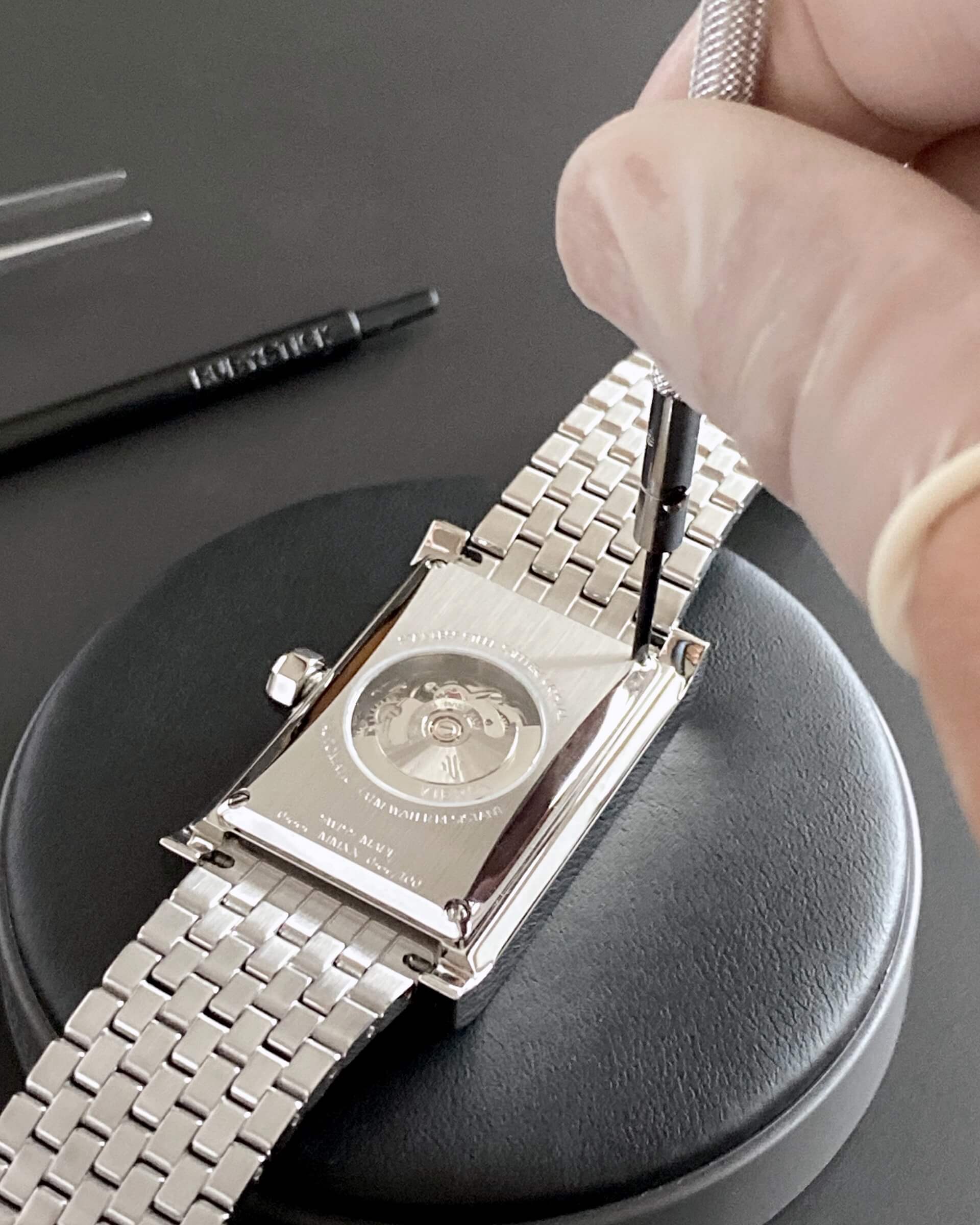 VIEREN silver rectangular watch caseback with Swiss automatic movement being opened with screwdriver and watchmaking tools